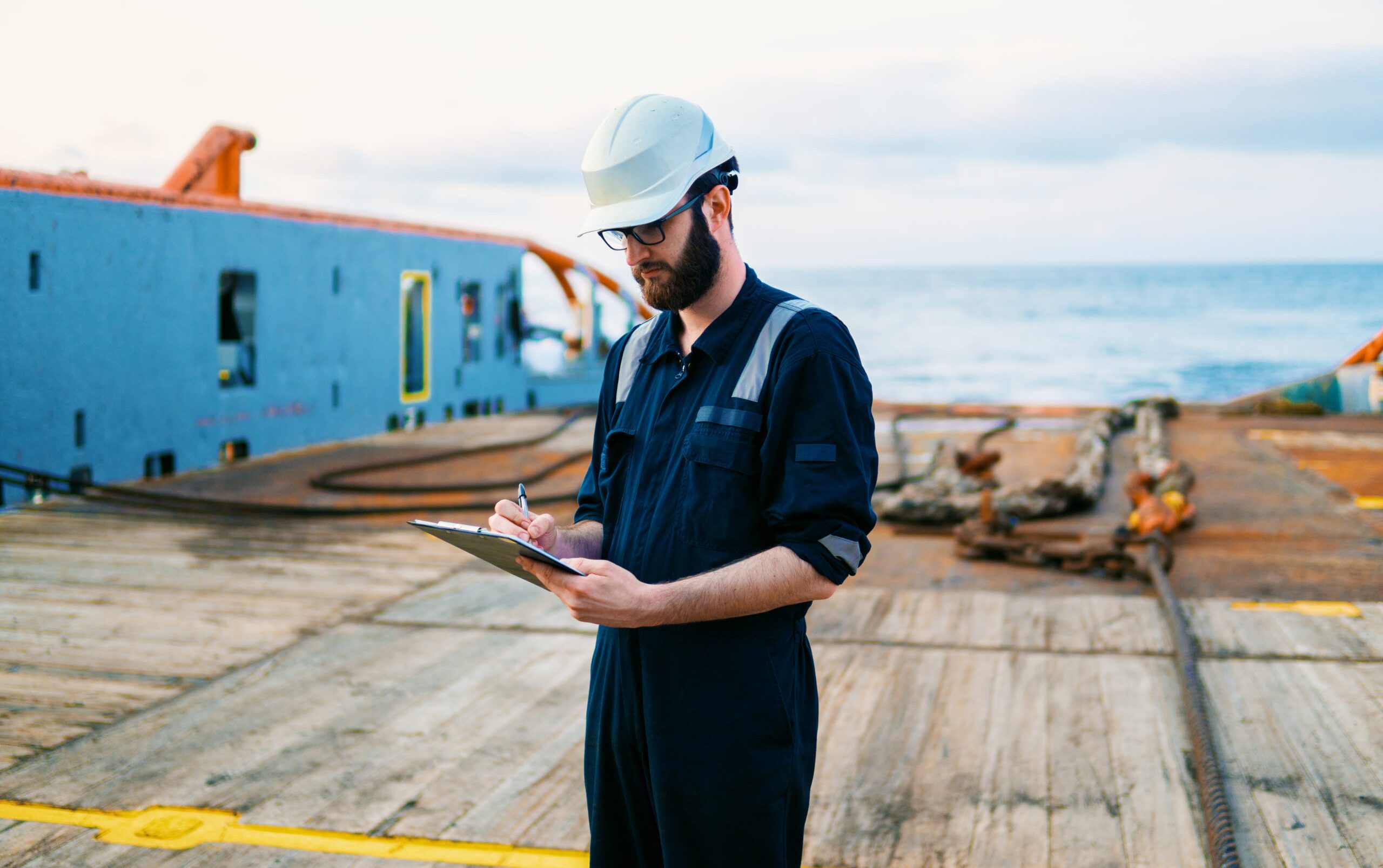 Deck Officer on deck of offshore vessel or ship , wearing PPE personal protective equipment. He fills checklist. Paperwork at sea